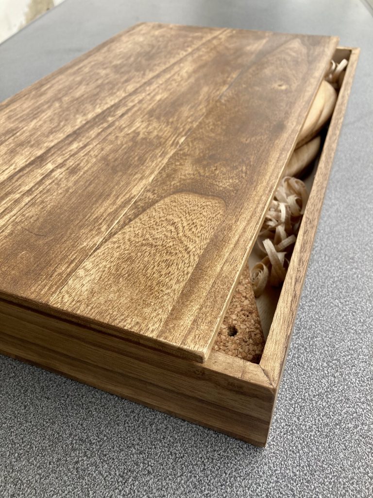 Open handcrafted wooden box revealing Frescobol paddles made from sustainable paulownia wood, surrounded by decorative wood shavings for an elegant presentation