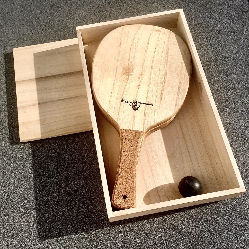 Single handcrafted Frescobol wooden paddle with a cork handle, displayed in a premium paulownia wood box alongside a blue-dot squash ball