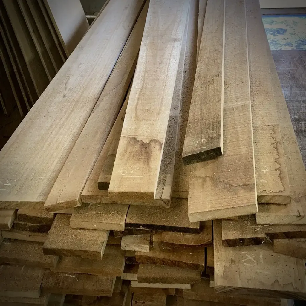 Stack of raw Paulownia wood planks, freshly sawn and marked for processing. The light and smooth texture of the wood is visible, showcasing its high quality