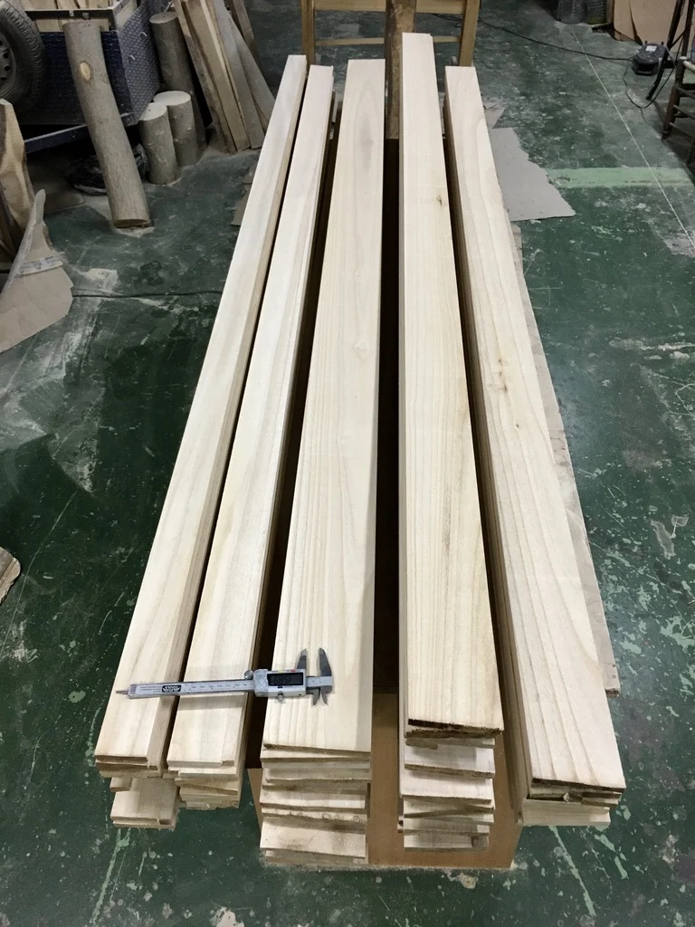 Neatly stacked planed Paulownia wood strips in a workshop, ready for use. A caliper is placed on one of the strips, indicating our precise measurement.