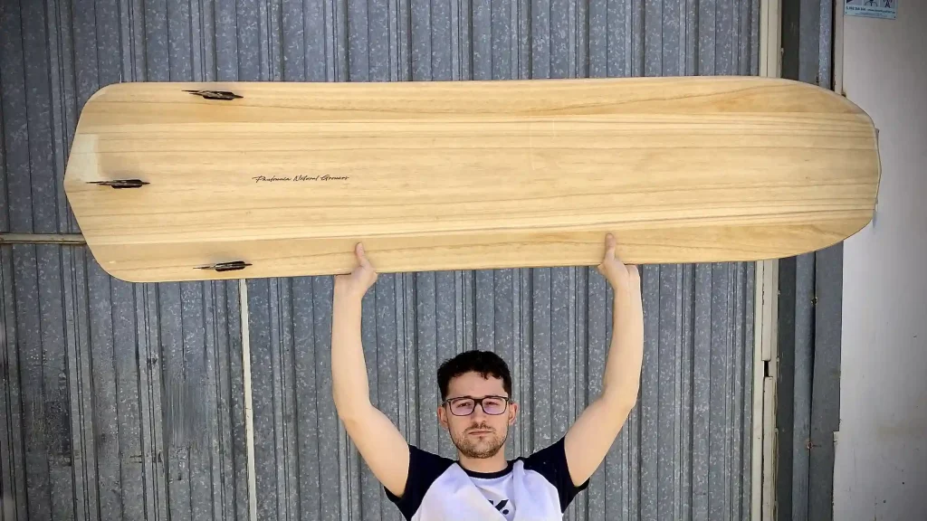 Handmade wooden kiteboard held up in front of the TK workshop